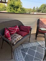 Brown resin wicker-like loveseat with cushions placed on a balcony, viewed from the front left side showing the cushions and armrest.