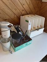 Photo of the lot showing the shelving unit with slatted dividers, Braun hand mixer, KitchenAid hand mixer, scale, and KitchenAid attachments on a box
