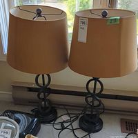 Two matching table lamps with metal bases and taupe shades by a window, showing overall condition and size