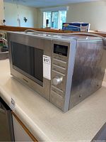 Side and front view of the Panasonic microwave on a kitchen counter showing stainless steel finish and control panel with buttons and dial.