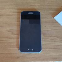 Samsung Galaxy S6 smartphone lying flat on wooden surface, screen off, front view showing Samsung logo on top.