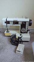 Front view of the Brother sewing machine including foot pedal and power cord on carpeted floor.
