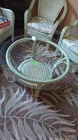 Glass top wicker coffee table with painted wicker base and woven lower shelf, shown with matching wicker armchairs.