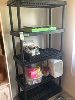 Front angled view of the black resin shelving unit showing four open grid shelves with various items placed on shelves (items not included in sale).
