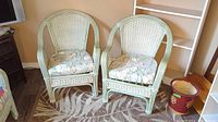 Two matching painted wicker chairs side by side with floral cushions, showing overall design and condition.