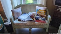 Full front view of painted wicker settee with floral cushion and miscellaneous contents on seat