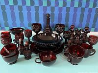 Overall view of Avon Cape Cod ruby red glassware set showing multiple pieces including dishes, cups, and shakers.