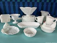 Full view of assorted milk glass items showing various bowls, creamers, plates and covered dishes in white milk glass with textured and embossed patterns.