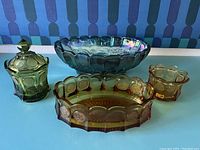 Four amber glass pieces, including covered jar, divided dish, small bowl, all Tiara Coin pattern, and an iridescent carnival glass footed bowl with grape motif.