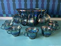 Front view of punch bowl surrounded by 12 matching cups on blue surface.