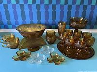 Full lot view showing amber Tiara glass cups, goblets, bowls, tray, and small dishes arranged on table.