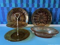 Three amber glass serving trays displayed against a blue patterned background including two round trays and one oval dish.