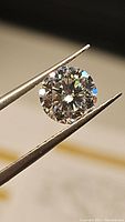 Close-up of round brilliant cut moissanite gemstone held with tweezers, showing sparkle and facets.