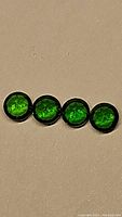 Four 4mm round cut deep electric green chrome diopside gemstones set against a beige background, showing color and cut.