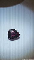 Photo of the pear-shaped deep purple sapphire gemstone on light background highlighting its color and facets.
