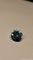 Close-up image of round cut Swiss Blue Topaz with lagoon blue color and detailed facets under lighting, showing clarity and cut quality.