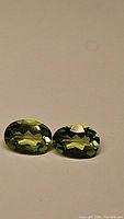 Pair of apple green Peridot gemstones shown from a slight top angle on neutral background.