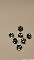 Seven round cut aqua blue teal sapphires arranged on a neutral background showing clarity and color.