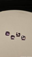 Four purple cushion checkerboard cut amethyst gemstones arranged on a flat surface showing color and cuts.