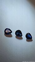 Three deep blue pear-shaped sapphires laid on a white surface showing their shape and color.
