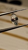 Close-up photo of fancy marquis cut moissanite gemstone held by tweezers showing shape and clarity.