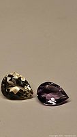 Pair of natural pear cut golden citrine and purple amethyst gemstones on neutral background.