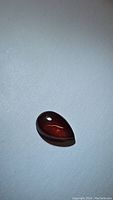Pear-shaped cabochon garnet gemstone in cherry red color on a white surface, showing glossy finish and smooth polish.