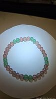 Top down view of a round stretchy bracelet with alternating clusters of pink strawberry quartz and green aventurine beads on a white background.