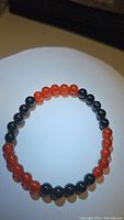 Clear top-down view of the bracelet showing alternating beads of bright orange Carnelian and black Onyx on an elastic cord.