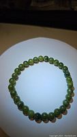 Photo of green jade bead bracelet arranged in a circle on a white plate, showing round polished beads with an elastic band.
