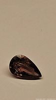 Pear shaped purple tourmaline gemstone resting on a neutral background showing facets and polish.