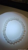 Top view of the natural white jade bead stretchy bracelet arranged in a circular shape on plain background under bright lighting showing bead size and color.