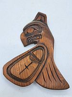 Top side of the carved wooden panel showing Thunderbird design with carved details and medium brown wood finish.