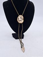 Full front view of the bolo tie displayed on a black stand showing the entire cord and central carved piece.