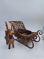 Miniature wooden sleigh with woven structure and a carved wooden reindeer standing beside it.