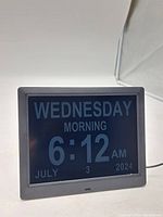 Front view of the digital calendar day clock showing "WEDNESDAY MORNING 6:12 AM JULY 3 2024" on the screen.