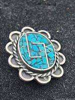 Front close-up showing oval turquoise mosaic inlaid in sterling silver with geometric silver design and floral border.