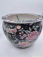 Photo of the vase exterior showing black background with detailed pink flowers and green leaves painted decoration.