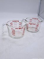 Pair of clear Pyrex glass measuring cups with red measurement markings showing cups, ounces, and milliliters.