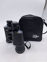 Photo showing Tasco Zip binoculars with attached strap and black carry case with Tasco Zip logo.