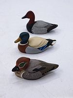 Three small vintage decorative duck decoys with distinct hand-painted details on white background.