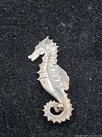 Front view of vintage 1960s sterling silver seahorse pin with detailed engraving and curled tail.
