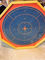 Full view of vintage Crokinole board showing octagonal wooden frame and blue playing surface with scoring zones marked in red and orange.