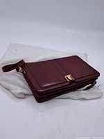 Side view of burgundy leather purse with wrist strap and gold clasp showing overall condition.