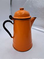 Vintage orange enameled campfire coffee pot with hinged lid and black handle photographed from the side.
