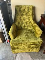 Front view of an antique green velvet upholstered chair showing tufted backrest and padded arms