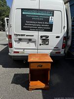 Full front view of vintage wooden night stand positioned against white vehicle door.