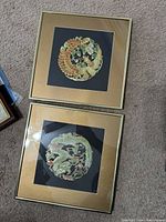 Two framed Asian paper cut dragon artworks shown together on carpet floor, showing overall condition and framing.
