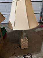 Lamp with shade attached showing carved stone base and cream fabric shade in a garage setting.