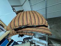 Three large throw pillows stacked one on top of another displaying their multicolor striped woven fabric.